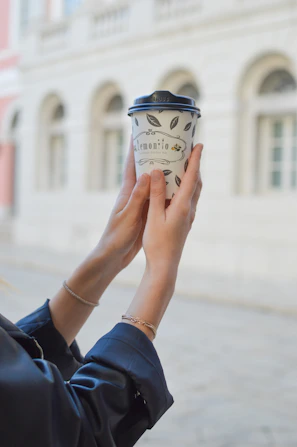 Casual street scene showing a hand adorned with yunka jewelry holding a coffee cup.