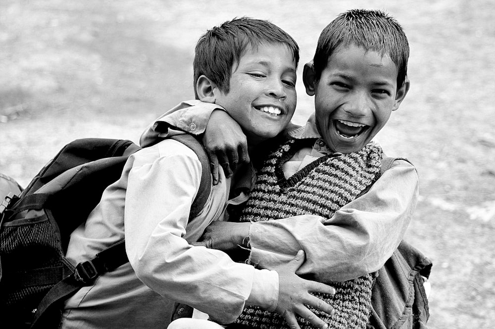 grayscale photography of two boys hugging while laughing