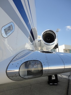 Close-up view of a jet engine on the side of an aircraft, showcasing metallic components with a reflection of the surrounding environment. The smooth, polished surface and aerodynamic design are highlighted against a clear blue sky.