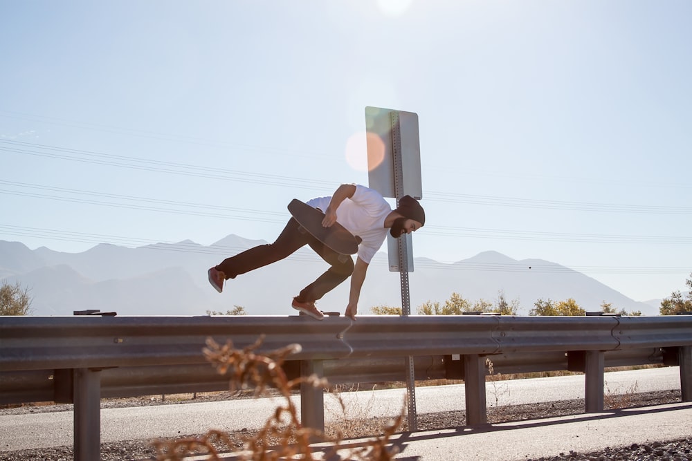 Hombre cruzando en la valla de la carretera mientras sostiene una patineta negra