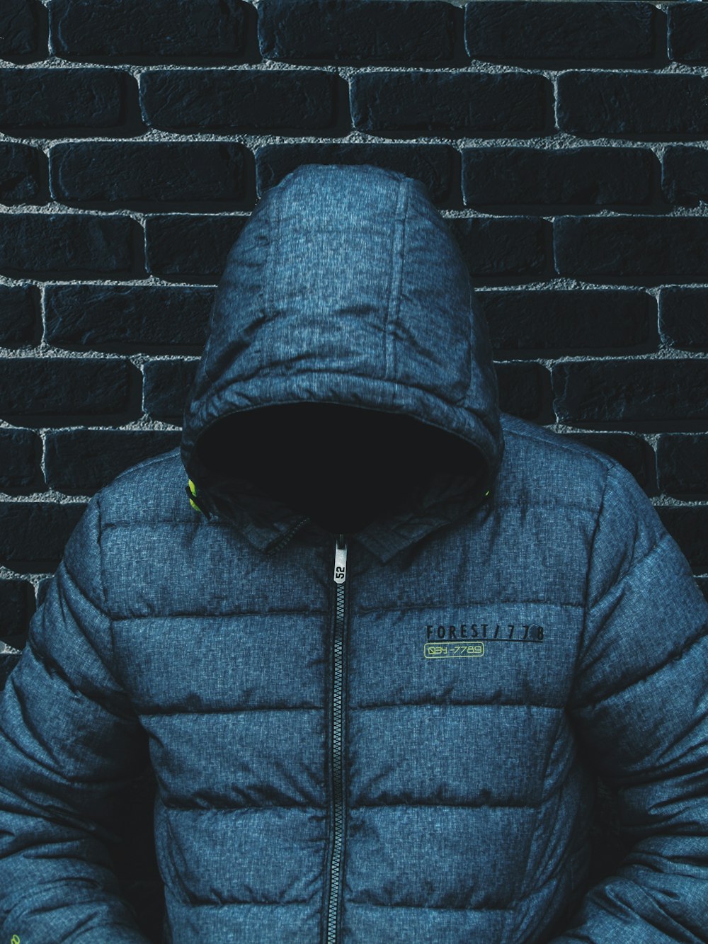 person with head down wearing blue zip-up jacket leaning on wall