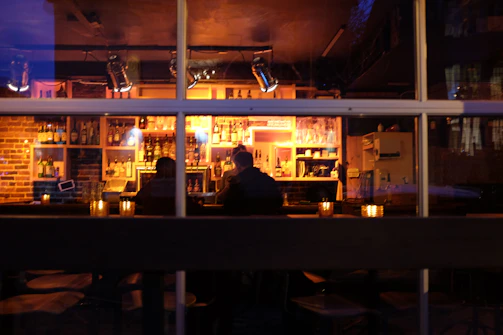 A cozy, dimly lit lounge where two people share an intimate conversation over drinks.