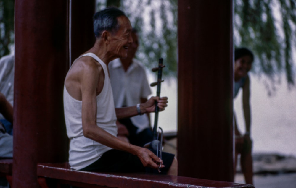 shallow focus photography of a man playing string instrument while sitting on a bench