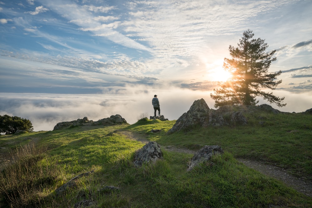 personne debout au sommet de la montagne sous un ciel nuageux