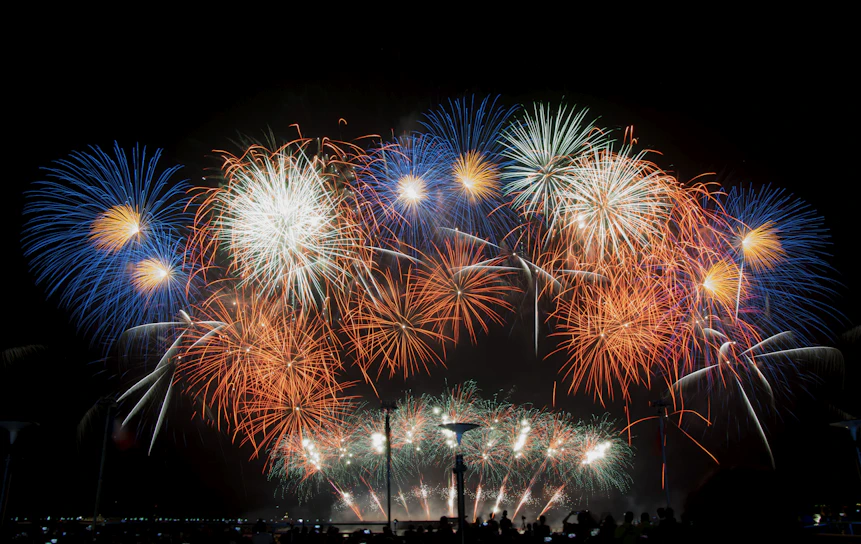 A vibrant burst of colorful fireworks lighting up the night sky over a festive crowd.