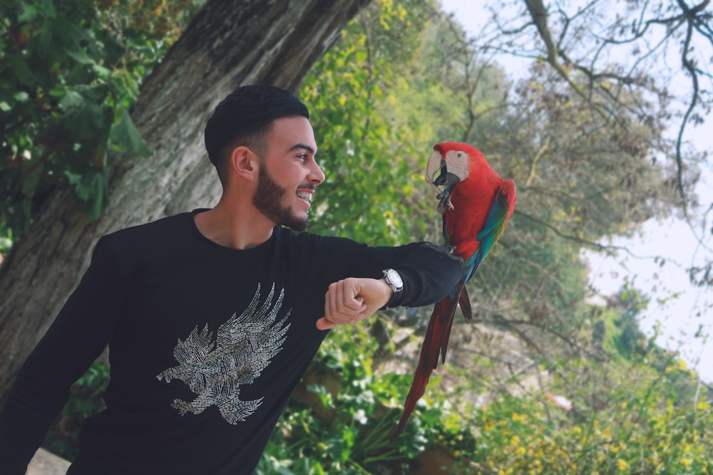 man in black crew neck shirt holding red and blue bird
