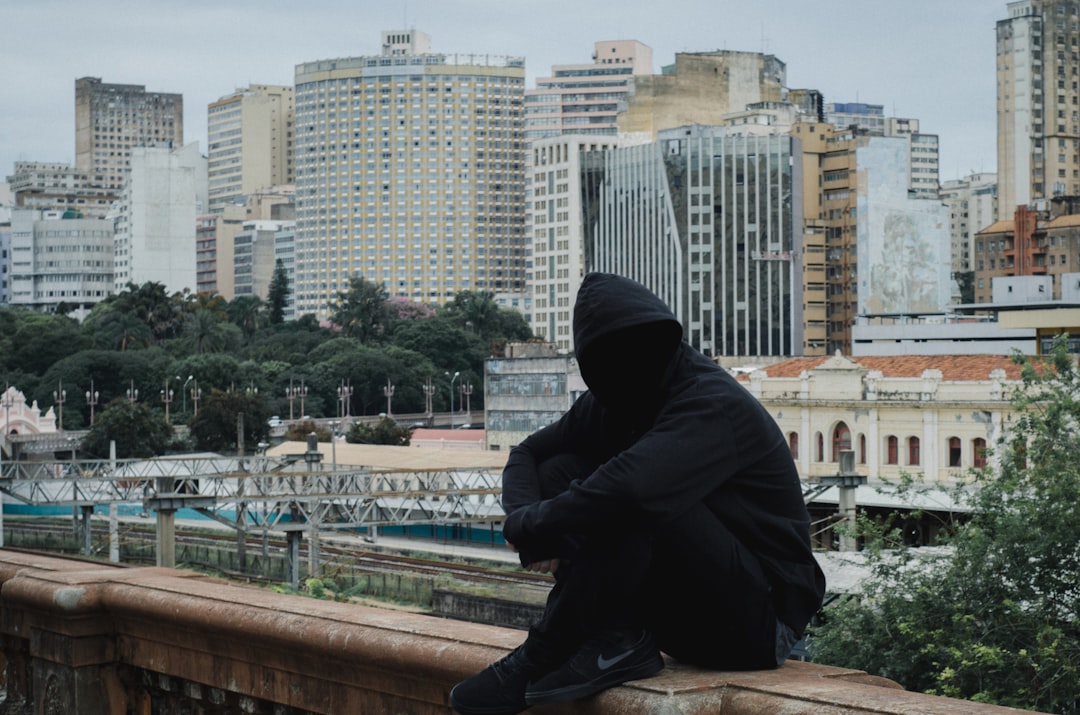 man wearing hooded jacket sitting on beige concrete