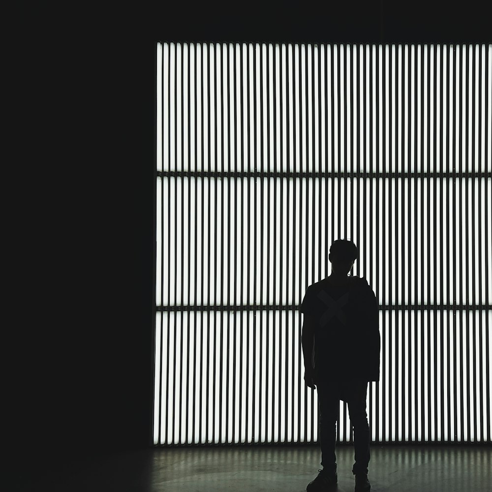 silhouette photo of a person standing near wall in dark room