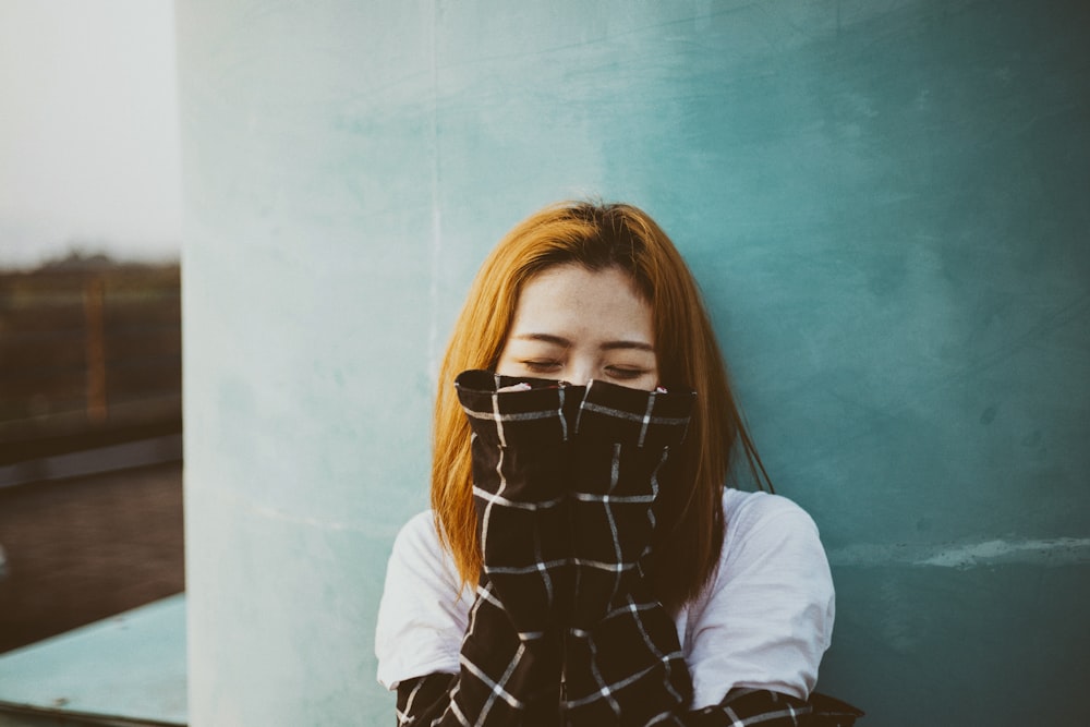 woman leaning on wall covering her mmouth