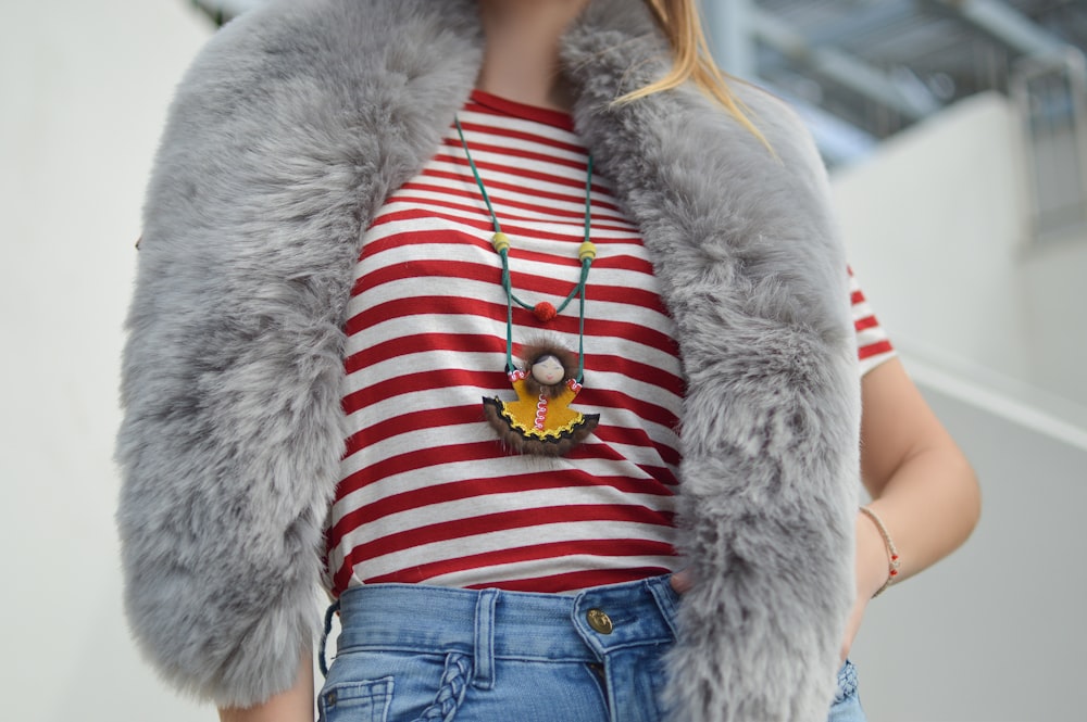 Donna che indossa t-shirt girocollo a righe rosse e bianche e pantaloni in denim blu con sciarpa in pelliccia sintetica grigia durante il giorno