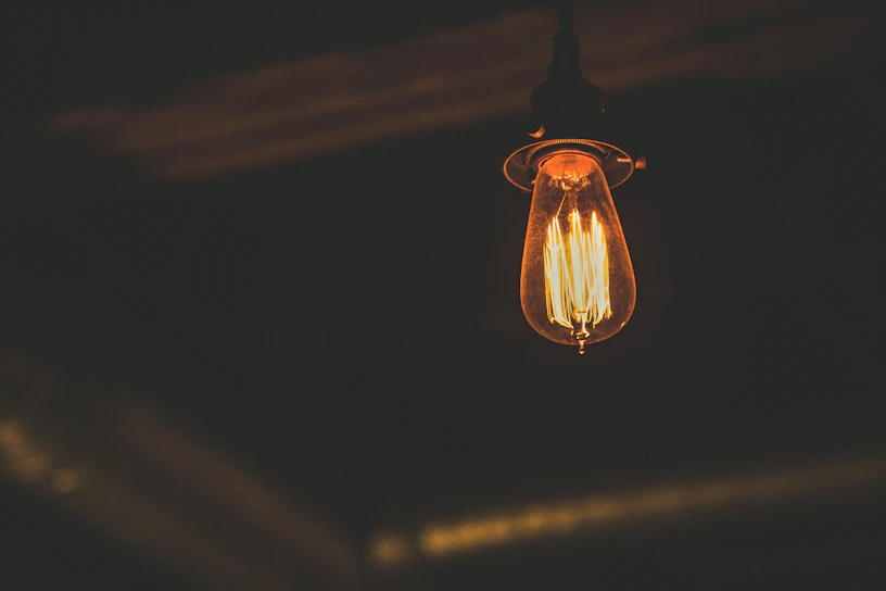 A close-up of a vintage Edison-style filament light bulb glowing warmly in a dim room.