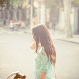 Model walking confidently down a sunlit street wearing a flowing midi dress with subtle floral detailing.
