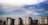Several modern apartment buildings with numerous windows and balconies stand under a vast, partly cloudy sky. The architecture reflects urban residential structures, featuring muted colors that blend harmoniously with the environment.