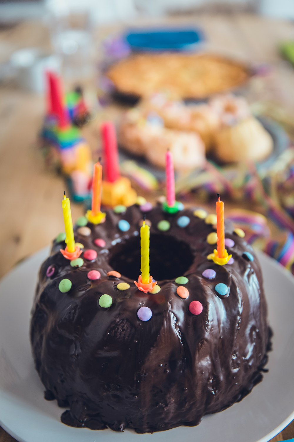 A chocolate covered bundt birthday cake with coloured candy and candles on top