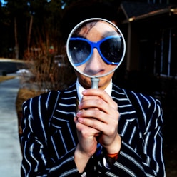 person using magnifying glass enlarging the appearance of his nose and sunglasses