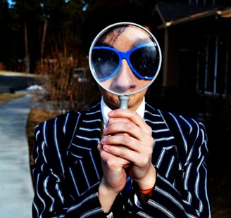 person using magnifying glass enlarging the appearance of his nose and sunglasses