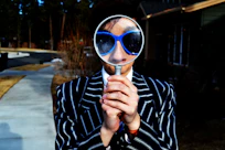 person using magnifying glass enlarging the appearance of his nose and sunglasses