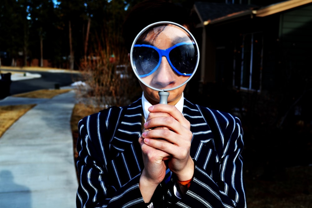 person using magnifying glass enlarging the appearance of his nose and sunglasses