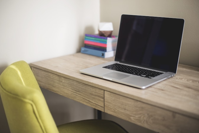 silver and black laptop computer on brown wooden desk beside green leather chair