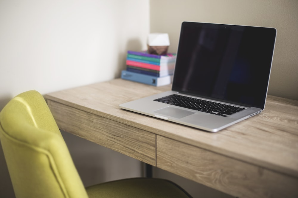 ordinateur portable argenté et noir sur un bureau en bois brun à côté d’une chaise en cuir vert