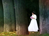 A candid shot of a bride holding a terracotta and sand-toned bouquet, sunlight filtering through trees.