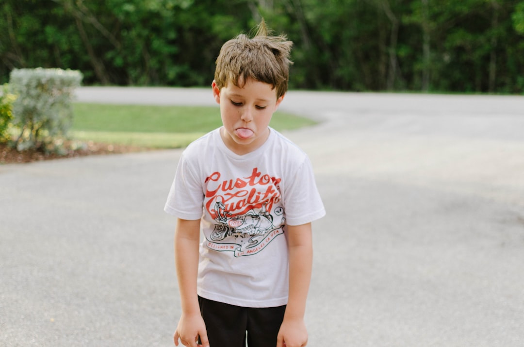 boy standing on gray concrete road while tongue out