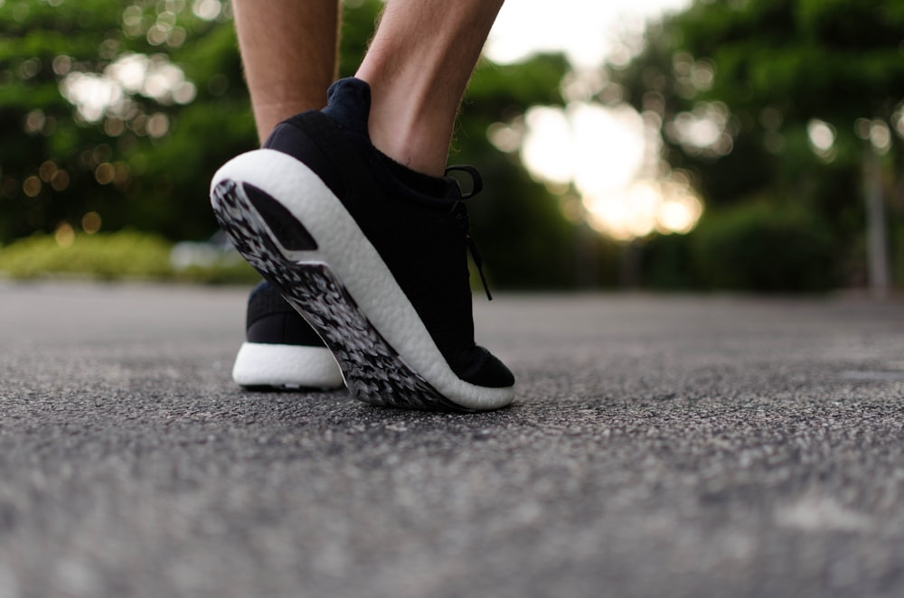 The sole of a pair of black and white shoes, taken from close up as someone lifts their foot to walk.