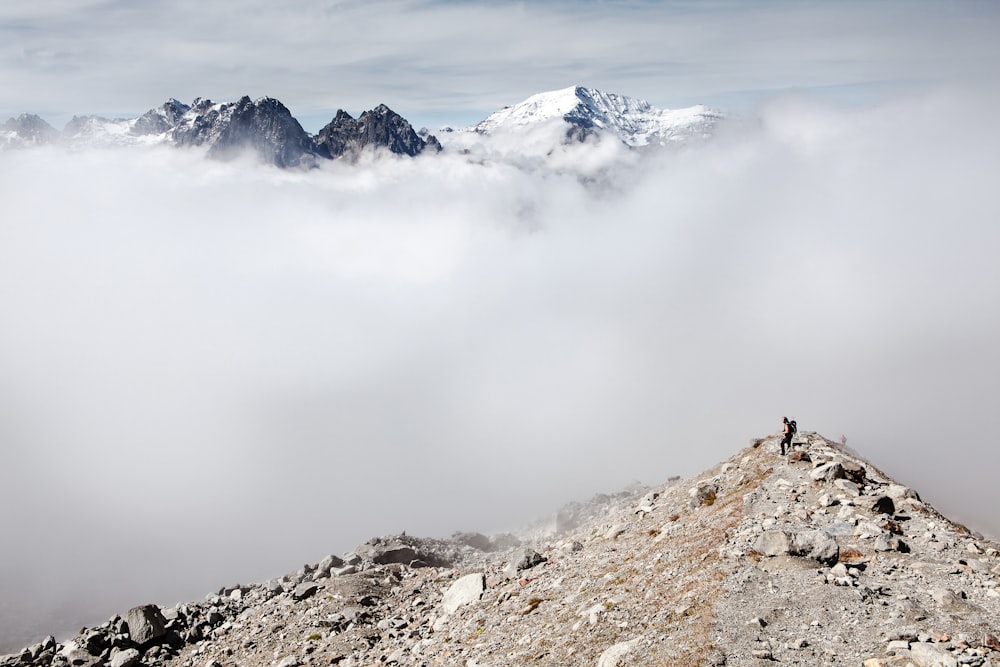 person standing on peak front of white clouds and ice-capped mountain
