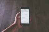 A hand holding a smartphone in a dimly lit environment, displaying text related to mobile optimization. The focus is on the smartphone screen, and the background is a blurred wooden surface.