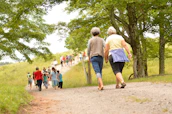 A group of smiling seniors enjoying a guided outdoor walk surrounded by lush greenery.