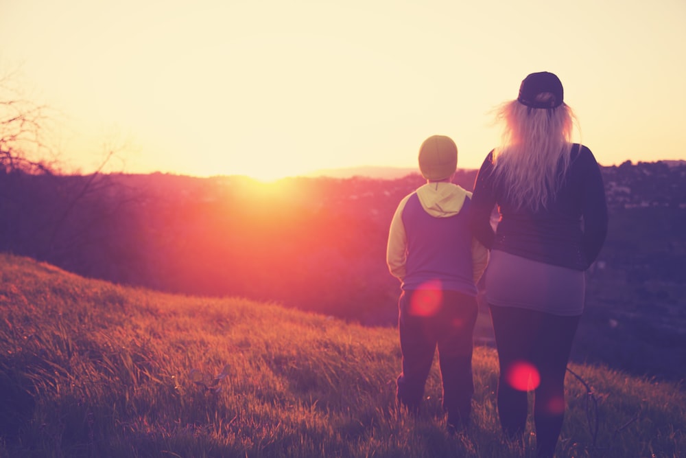 silhouette photo of woman standing beside a child on grass field