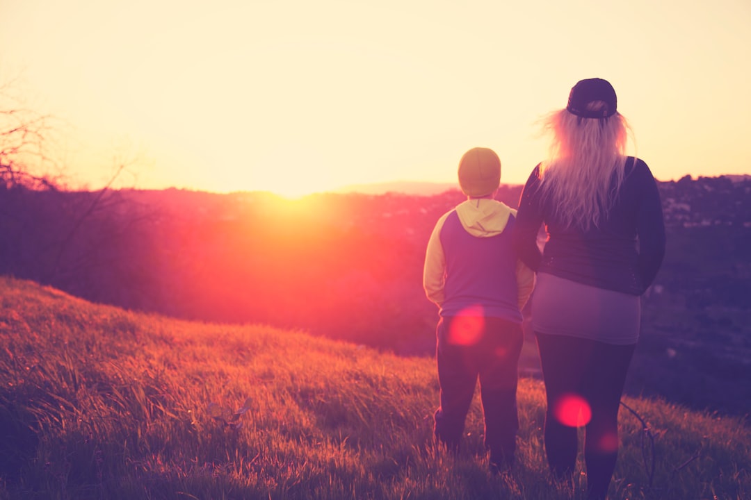 silhouette photo of woman standing beside a child on grass field