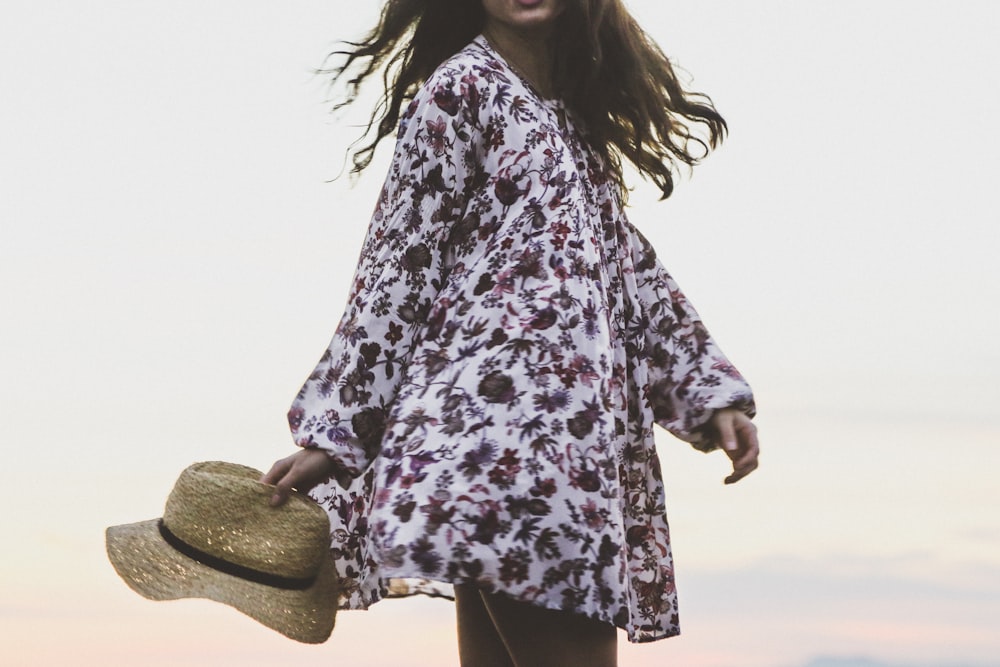 woman wearing white and brown floral long-sleeved shirt while holding brown fedora hat