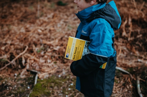A person wearing a blue and black jacket is holding a map titled 'New Forest' while standing in a natural environment with brown, dry foliage in the background.