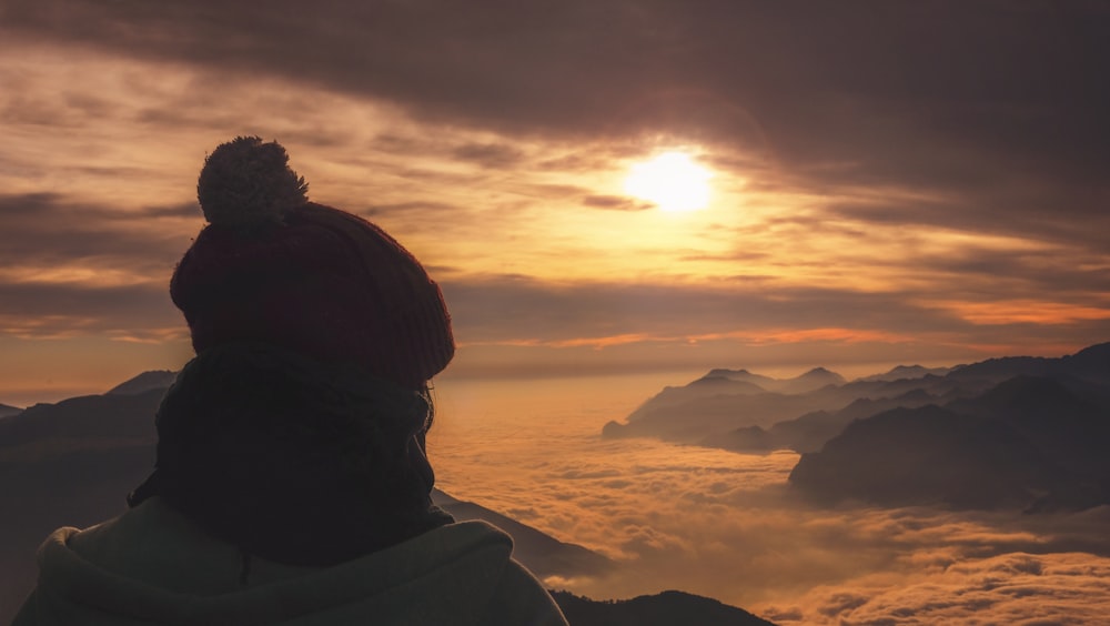 person in red knit cap leaning on sea of clouds