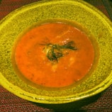 A cozy mug filled with creamy tomato soup garnished with a swirl of cream and herbs.