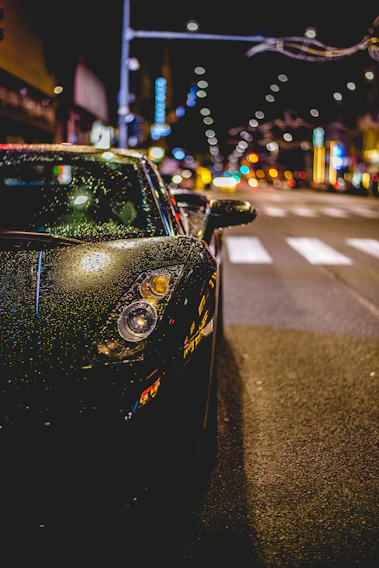 A sleek car covered with vibrant advertising decals parked on a busy city street at sunset.