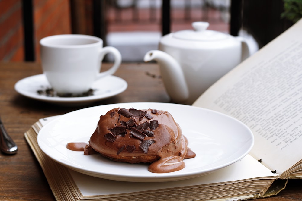 Dessert au chocolat sur un livre ouvert avec une théière et une tasse de thé en arrière-plan