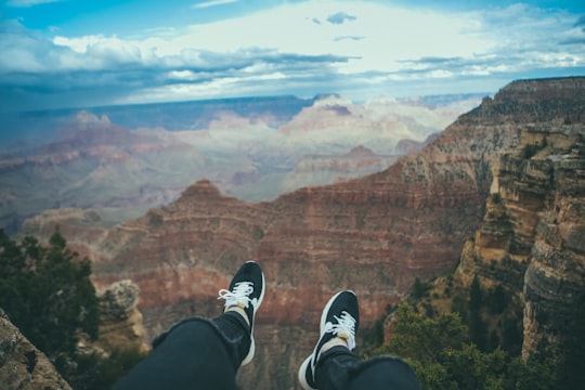 person sitting looking through mountain taken under white clouds during daytime in Grand Canyon National Park United States