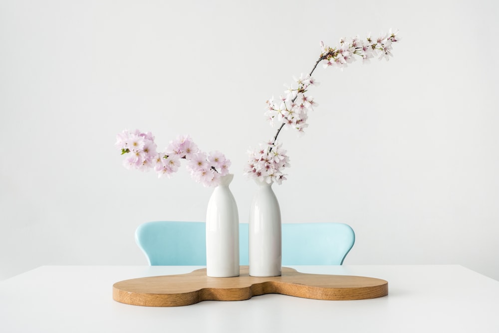 two pink petaled flowers in white vases on brown wooden surface