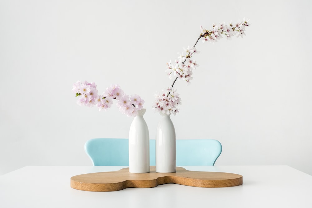 deux fleurs aux pétales roses dans des vases blancs sur une surface en bois brun
