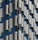 A close-up view of a building facade featuring an intricate pattern of undulating, metallic panels that create a wave-like effect. The design incorporates both reflective and matte surfaces, allowing light to play across the structure, revealing subtle shades of gray and blue.