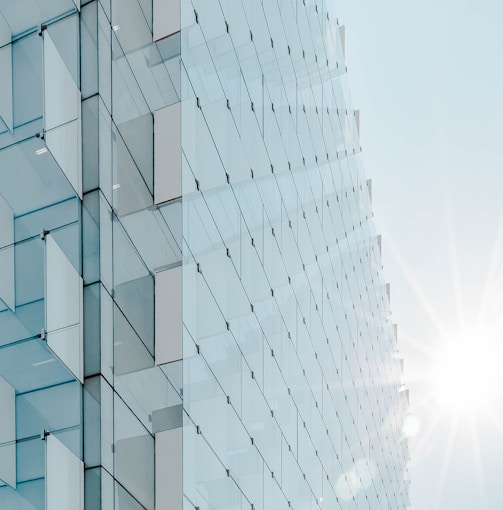 glass panel high-rise building under blue sky with sun raise