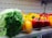 A shelf in a grocery store displays fresh vegetables, including a large, leafy green cabbage wrapped in plastic, and an assortment of vibrant bell peppers in red, yellow, and orange hues.