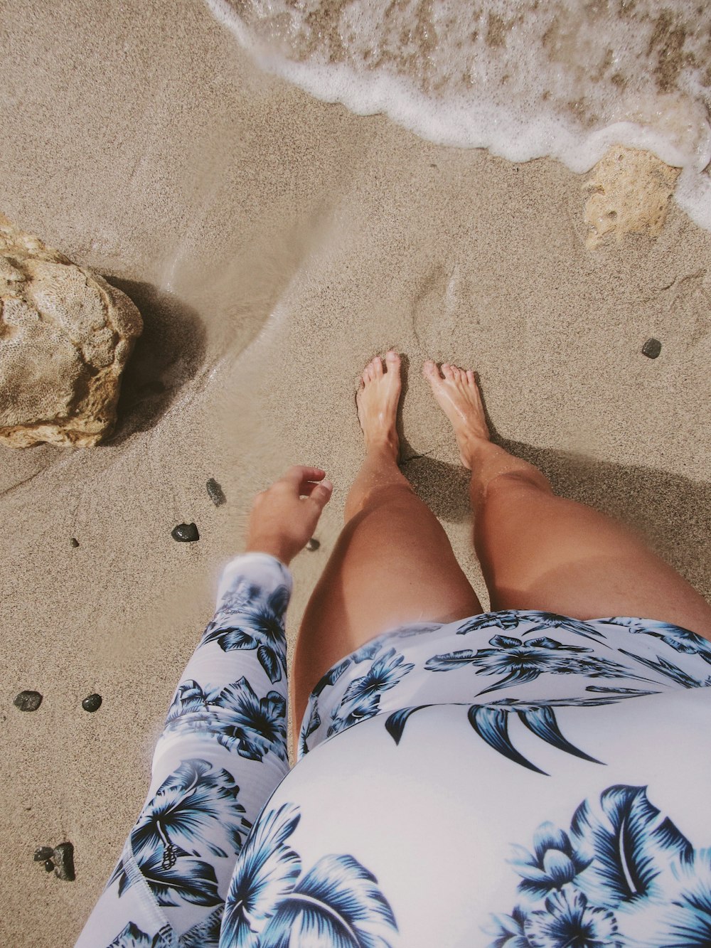 A perspectiva de uma mulher olhando para seus pés enquanto está em pé em uma praia de areia.