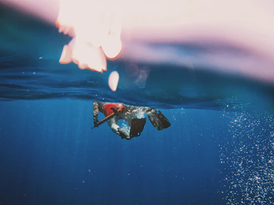 Close-up of a diver in full gear navigating a deep ocean site with beams of light piercing the water.