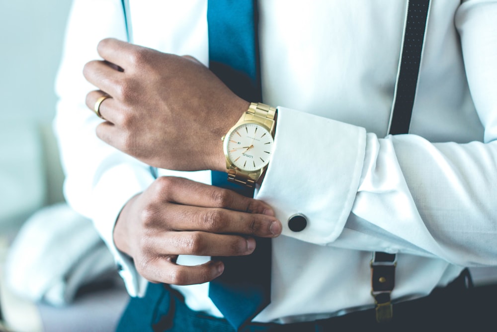 A man in a gold watch adjusting the cuffs of his white shirt