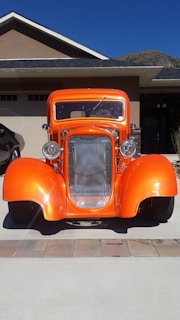 A vibrant orange car duster in action, gently wiping dust off a shiny blue car under a clear sky.