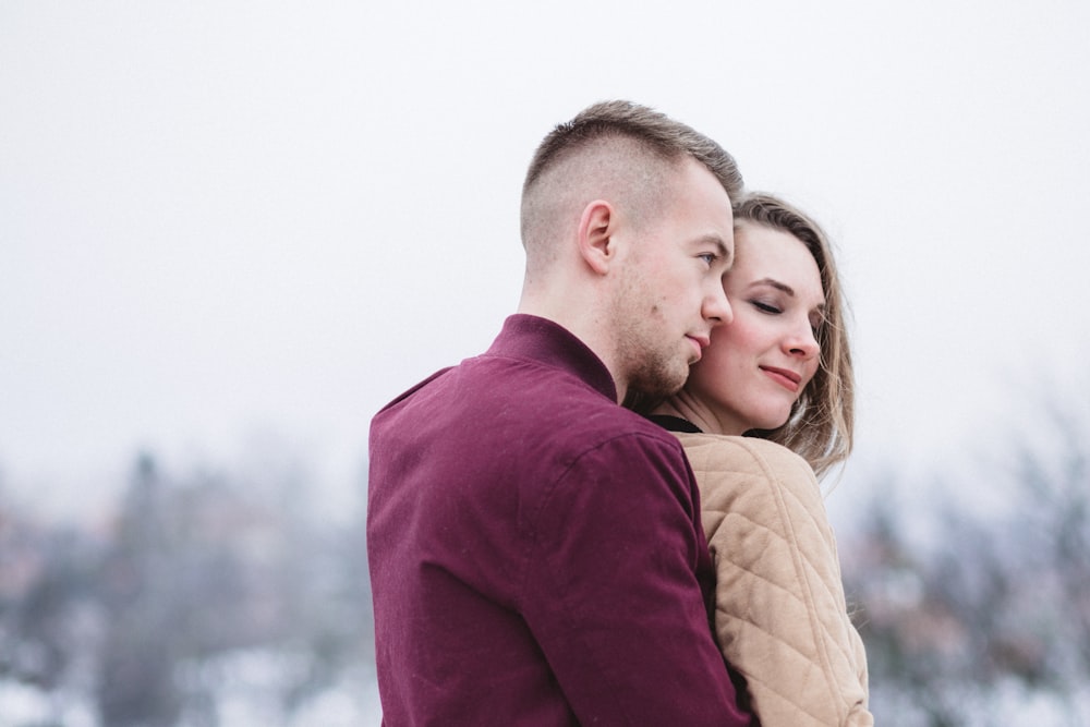 man hugging woman while standing on snowy weather