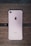 A rose gold smartphone with an Apple logo on the back is placed on a wooden surface. The device is lying flat, showing its camera, flash, and antenna lines.